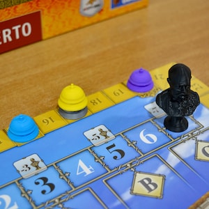 May include: A board game with a blue and yellow game board. The game pieces include a black bust, and blue, yellow, and purple cone-shaped pieces. The numbers 3, 4, 5, and 6 are visible on the board.