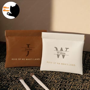 May include: Two personalized leather pouches with the names Jordan and Wilma, each with a monogrammed initial and the phrase "Rose of No Man's Land."