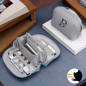 May include: A light blue travel organiser with multiple compartments for electronics and accessories. The organiser is open and shows a variety of items, including a power bank, charging cables, and a wireless mouse. The organiser has a zipper closure and is made of a durable fabric.