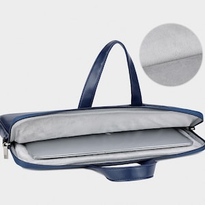 May include: A navy blue laptop bag with a handle and a zipper closure. The bag is open, revealing a laptop inside. The interior is lined with a soft, gray material. The bag has a handle for carrying.