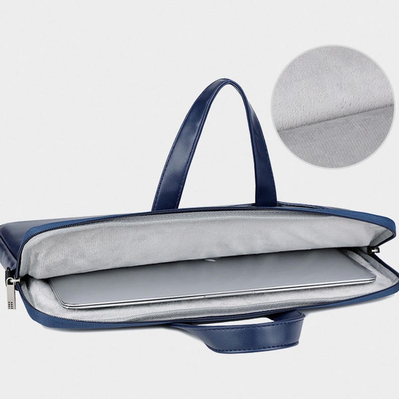 May include: A navy blue laptop bag with a handle and a zipper closure. The bag is open, revealing a laptop inside. The interior is lined with a soft, gray material. The bag has a handle for carrying.
