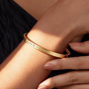 May include: A gold-colored bangle bracelet with the inscription "BEAUTIFUL GIRL, YOU WERE MADE TO DO GREAT THINGS." The bracelet is worn on a wrist, showcasing its elegant design and inspirational message. The bracelet is a simple, yet stylish accessory.