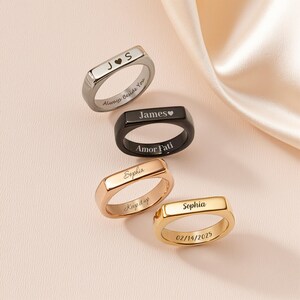 Puede incluir: Cuatro anillos personalizados en plata, negro, oro rosa y oro. Cada anillo presenta texto grabado, incluyendo nombres, fechas y frases como "Always Beside You" y "Amor Fati". Los anillos tienen un diseño rectangular.