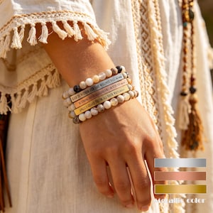 May include: A stack of beaded bracelets with metallic gold, copper, and silver accents. Each bracelet features inspirational text: "GOD IS WITHIN HER SHE WILL NOT FAIL," "BE STRONG AND COURAGEOUS," and "ANGELS GUARD YOU IN ALL YOUR WAYS."