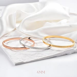 May include: Three bangle bracelets in rose gold, silver, and gold, each with engraved text. The rose gold bracelet says "Sophia ❤️ Tom", the silver bracelet says "Don't Let The Hard Days Win", and the gold bracelet says "BEAUTIFUL GIRL, YOU WERE MADE TO DO GREAT THINGS". The bracelets are 4mm wide.