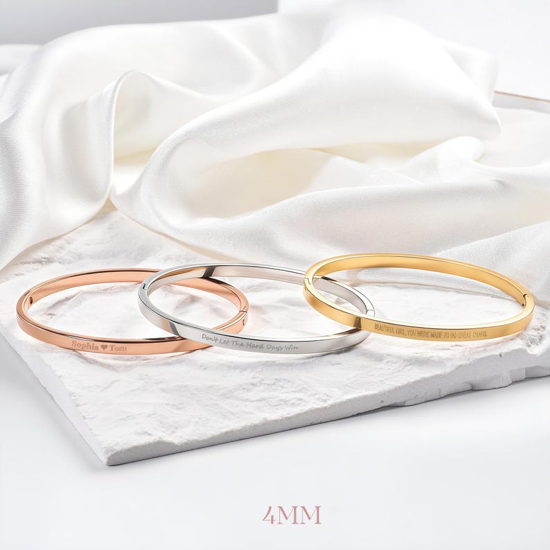May include: Three bangle bracelets in rose gold, silver, and gold, each with engraved text. The rose gold bracelet says "Sophia ❤️ Tom", the silver bracelet says "Don't Let The Hard Days Win", and the gold bracelet says "BEAUTIFUL GIRL, YOU WERE MADE TO DO GREAT THINGS". The bracelets are 4mm wide.