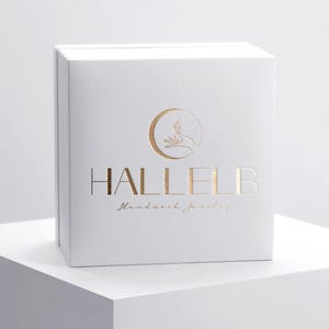 May include: A white box with gold lettering and a logo featuring a crescent moon and hand. The box has the brand name "HALLELB" and the words "Handwork jewelry" in a script font.