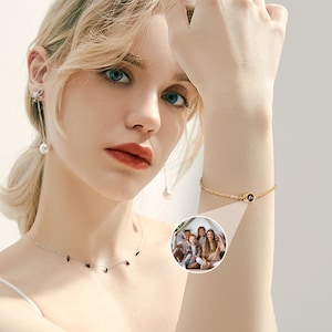 May include: A gold chain bracelet with a small, round, red gemstone charm. The bracelet is on a person's wrist.