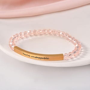 May include: A pink beaded bracelet with a gold bar charm that reads "You're unstoppable".