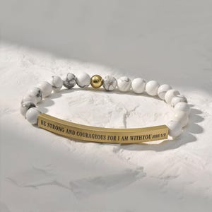 May include: White marble bead bracelet with a gold bar charm engraved with the text "BE STRONG AND COURAGEOUS FOR I AM WITH YOU JOSH 1:9".