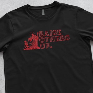 May include: Black t-shirt with a red graphic of a person raising another person up with the text "RAISE OTHERS UP."