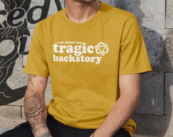 May include: A mustard yellow t-shirt with the text "ask about my tragic backstory" and a white dice graphic.