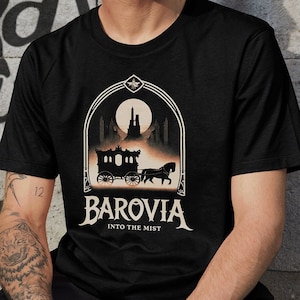May include: Black t-shirt with a graphic of a horse-drawn carriage and a castle in the background. The text "Barovia Into The Mist" is printed below the graphic.