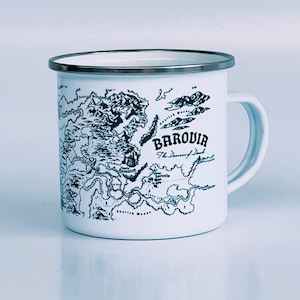 May include: White enamel mug with a silver rim and handle. The mug features a black and white map design with the word "Barovia" and the text "The Domain of Dread". A classic camping-style mug.