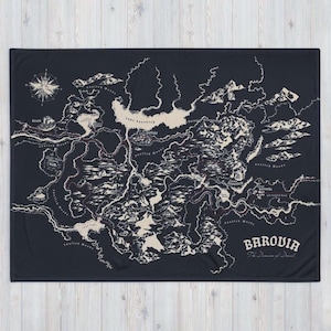 Puede incluir: Una manta negra con un diseño de mapa detallado en crema y rojo. El mapa incluye características geográficas, nombres de lugares y una rosa de los vientos. La palabra "Barovia" se muestra de forma destacada.
