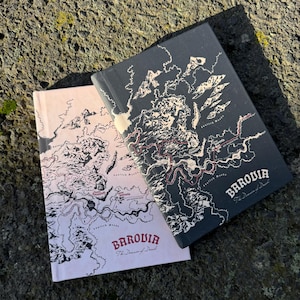 May include: Two hardback books with map designs. One book is pale pink, the other is dark grey. Both books have the word "Barovia" and the phrase "The Domain of Dread" printed on the cover in a serif font.