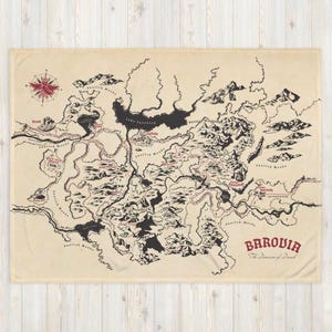 May include: A beige throw blanket featuring a detailed map of Barovia, with black illustrations of mountains, rivers, and forests. The map includes the text "Barovia" in red, and a compass rose.