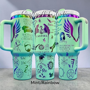 May include: Three mint green insulated tumblers with rainbow accents and handles. Each tumbler features various graphics and text, including phrases like "Driver Picks the Music" and "Hello Boys." The tumblers are decorated with images of wings, symbols, and characters.