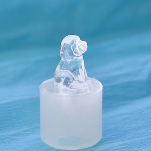 May include: A clear glass dog figurine sitting on a white silicone mold. The figurine is detailed and realistic, with a sitting pose and a slightly tilted head.