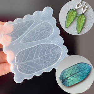 Puede incluir: Un molde de silicona transparente con cavidades en forma de hoja, sostenido por una mano. La imagen también muestra pendientes y un colgante en forma de hoja, ambos con tonos verdes y azules, sugiriendo un tema de joyería inspirado en la naturaleza.