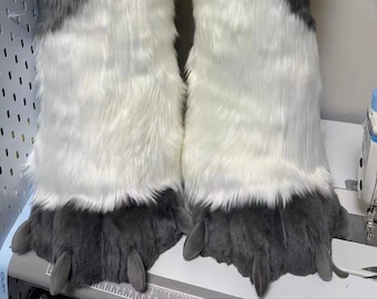 May include: A pair of white and gray furry paw-shaped leg warmers with black claws. The leg warmers are made of soft, plush fabric and are perfect for adding a touch of whimsy to any outfit.