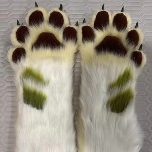 Op de afbeelding: Een paar witte, harige handpoppen met bruine pootkussens en groene poot afdrukken.