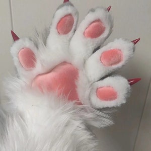 May include: A close-up of a plush paw in white and grey, featuring pink pads and sharp, red claws. The paw has soft fur and a realistic design, suitable for cosplay or costume use.