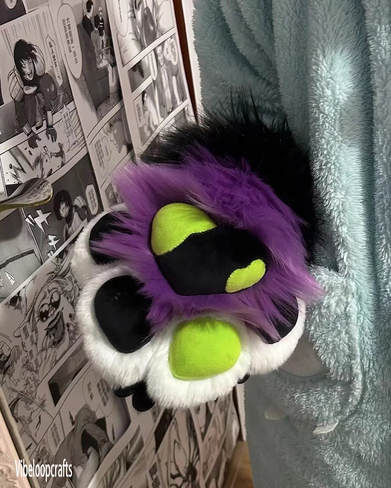 May include: A plush paw with black, white, purple, and green fur. The paw has three toes and a black pad.