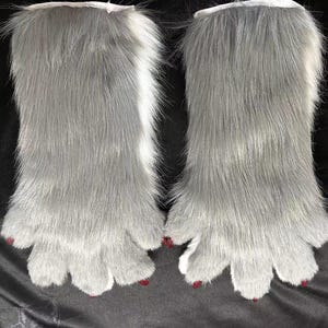 May include: A pair of grey faux fur paws with white cuffs and red painted claws. The paws have a realistic design with five toes each, and are likely part of a costume or cosplay accessory.