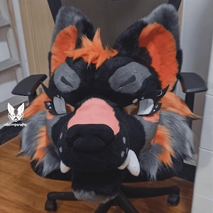 May include: A black and grey furry animal head with orange accents. The head has a black nose and white teeth. The head is on a black office chair.