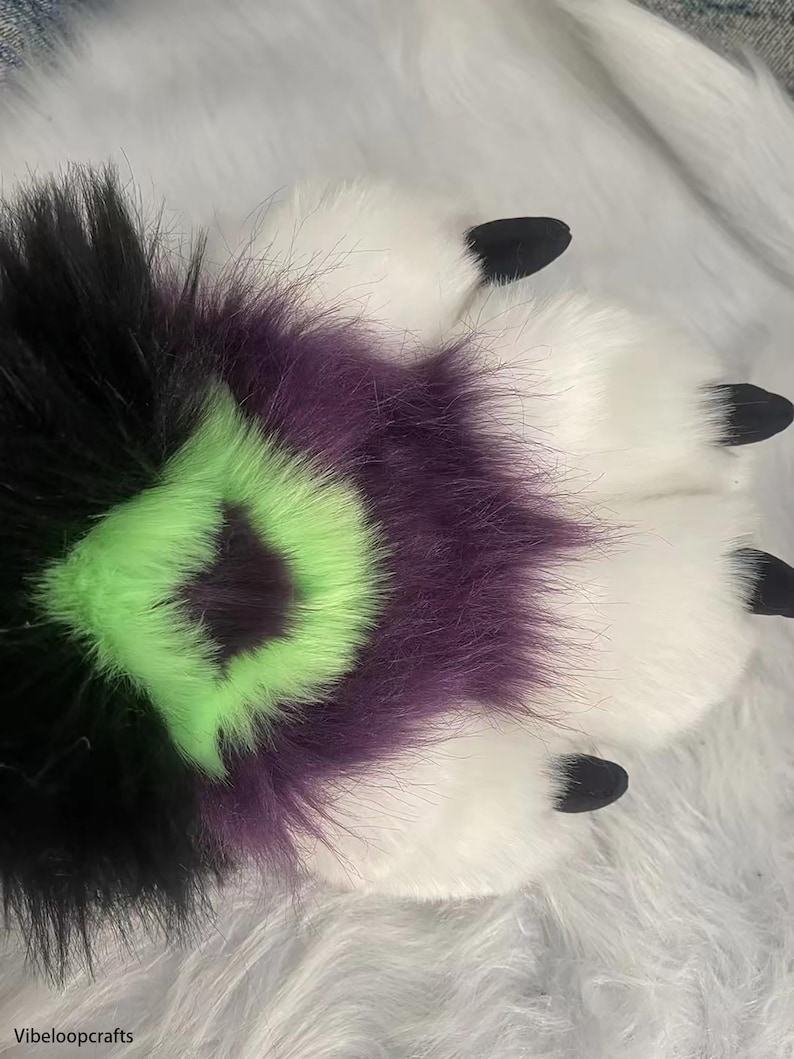 May include: A furry paw with black, purple, and green fur. The paw has black claws and is on a white fuzzy surface.