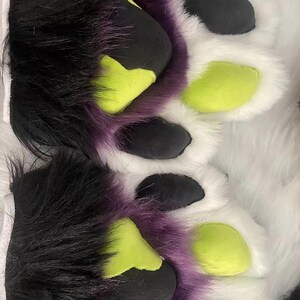 May include: A pair of furry paws with black, purple, and green accents. The paws are made of soft, plush fabric and have a realistic look.
