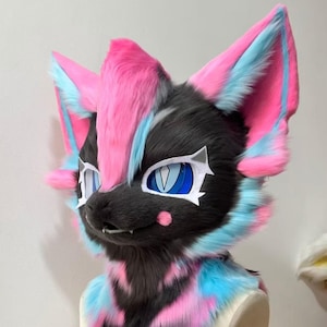 May include: A furry, stylized animal head with a black and gray base, accented with pink and blue fur. The ears and top of the head are pink, with blue accents. The eyes are blue with white accents. The overall design is vibrant and playful.