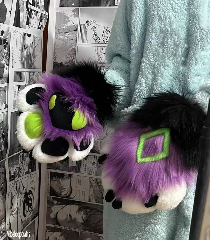 May include: A pair of purple and white furry paw hand puppets with black fur accents. One paw has a green diamond shape and the other has a green circle shape.