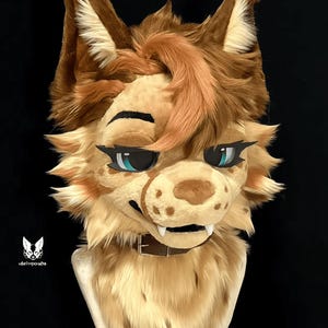 May include: A furry animal head with brown and tan fur, blue eyes, and a brown leather collar. The head is made of plush fabric and has a realistic appearance.