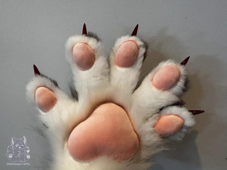 May include: A large, plush paw in white fur with grey detailing and pink pads. It has sharp, burgundy-coloured claws. The design resembles a large animal paw, possibly for a costume or novelty item. The paw is likely a prop.