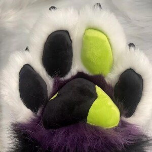 May include: A white furry paw with black and green paw pads. The paw pads are made of felt and have a stitched design.