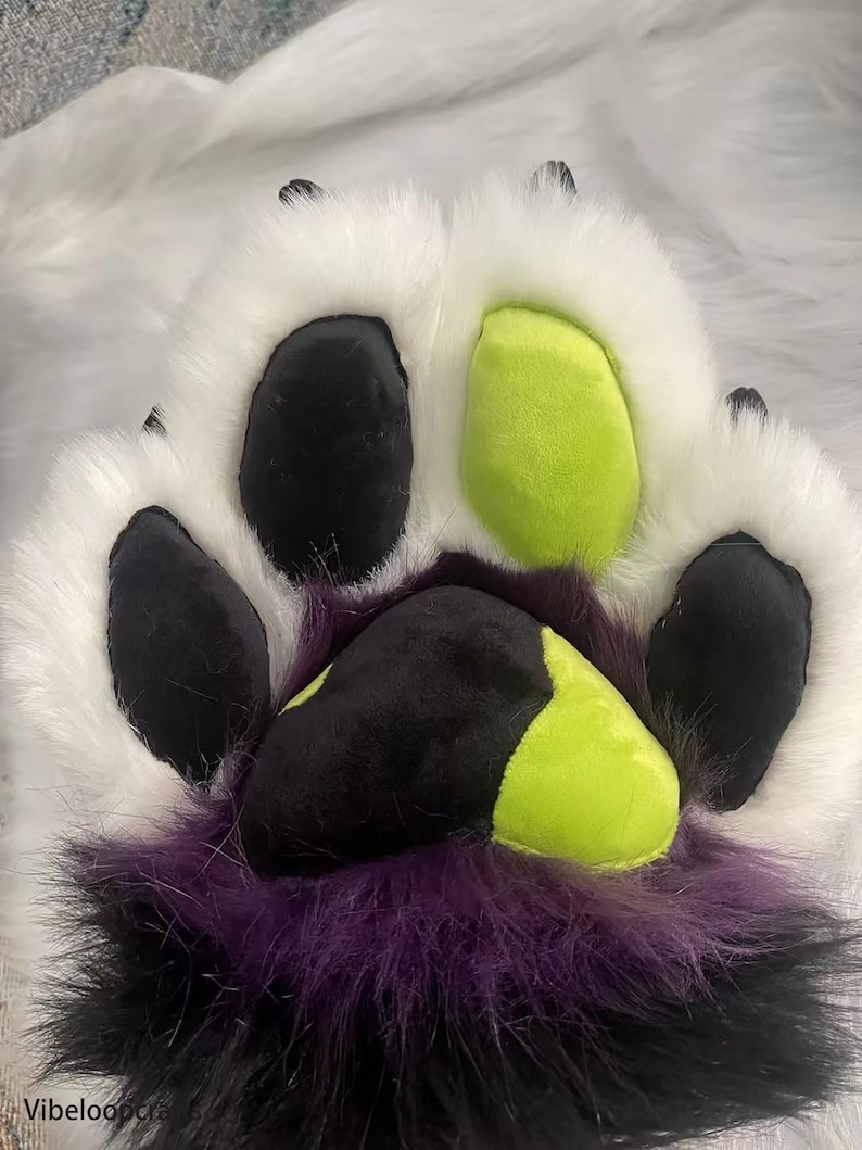 May include: A white furry paw with black and green paw pads. The paw pads are made of felt and have a stitched design.