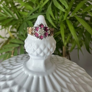 以下が含まれることがあります： 花の形をしたデザインの金と銀の指輪。花は小さなピンク色の宝石と中央に1つの大きな透明な宝石でできています。