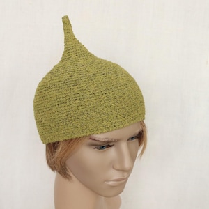 Puede incluir: Un sombrero verde claro, tejido a mano, con una parte superior puntiaguda. El sombrero tiene un aspecto texturizado y una base redondeada. El sombrero se muestra en una cabeza de maniquí. Es un accesorio único.