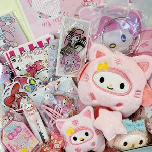 Puede incluir: Una bolsa de regalo rosa y blanca con temática de Hello Kitty llena de varios artículos, incluyendo un juguete de peluche Hello Kitty, un llavero Hello Kitty y una libreta Hello Kitty. La bolsa está decorada con personajes de Hello Kitty y las palabras "My Melody".