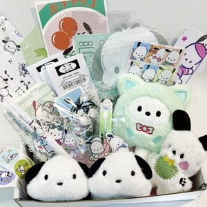 Puede incluir: Una caja de regalo llena de varios art&iacute;culos, incluyendo un juguete de peluche con una cara de gato verde y blanco, un juguete de peluche blanco y negro con una cara de gato, un llavero con un personaje de dibujos animados y una variedad de pegatinas y papeler&iacute;a. La caja est&aacute; decorada con un patr&oacute;n de lunares rosa y blanco.