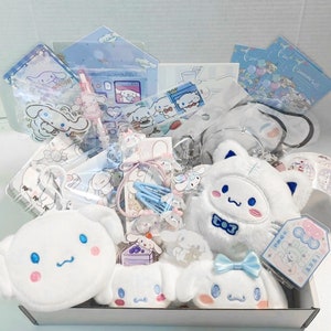 Puede incluir: Una caja blanca llena de varios art&iacute;culos de tem&aacute;tica azul y blanca, incluyendo un perro de peluche blanco con una pajarita azul, un bolso blanco con una cara bordada azul y una variedad de pegatinas, bol&iacute;grafos y accesorios para el cabello.