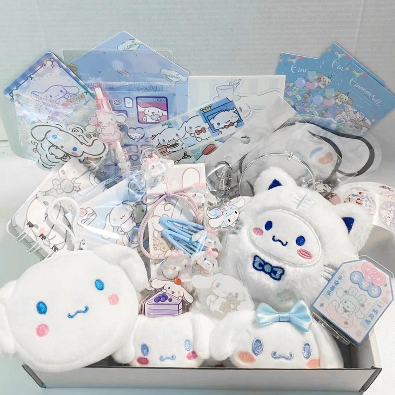 Puede incluir: Una caja blanca llena de varios art&iacute;culos de tem&aacute;tica azul y blanca, incluyendo un perro de peluche blanco con una pajarita azul, un bolso blanco con una cara bordada azul y una variedad de pegatinas, bol&iacute;grafos y accesorios para el cabello.