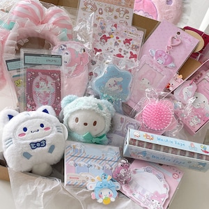 Op de afbeelding: Een roze en witte cadeaudoos gevuld met My Melody-kantoorbenodigdheden, pluche speelgoed en accessoires. De doos bevat stickers, een haarband, een sleutelhanger, een borstel, een notitieblok en een klein pluche speelgoed. De items zijn allemaal in tinten roze, wit en blauw.