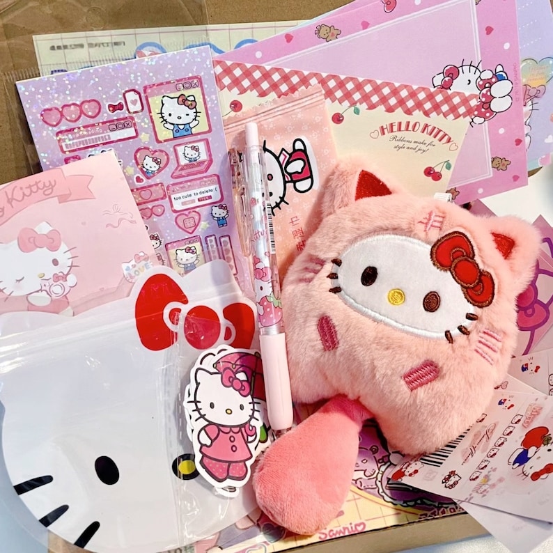 Puede incluir: Un peluche rosa de Hello Kitty con un lazo rojo y una cola a rayas rosa y blanca. El juguete est&aacute; rodeado de varios art&iacute;culos de papeler&iacute;a con tem&aacute;tica de Hello Kitty, incluidos pegatinas, blocs de notas y un bol&iacute;grafo.