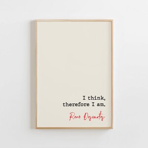 May include: Framed print with a cream background. The print displays the quote "I think, therefore I am" in black text, with the name "René Descartes" in red cursive. The frame is a light wood colour.