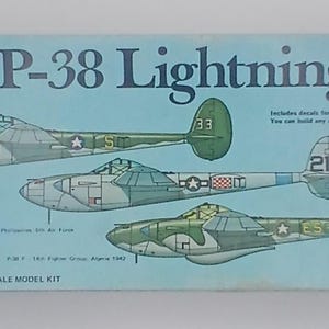Puede incluir: Caja de modelo a escala del avión P-38 Lightning. La caja es de color azul claro con ilustraciones de tres aviones diferentes. El texto "PROFILE SERIES" y "P-38 Lightning" se muestran de forma destacada. El kit es a escala 1/72.