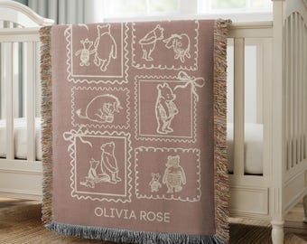 May include: A mauve-colored baby blanket with a Winnie the Pooh theme, featuring various characters in white framed illustrations. The blanket has a fringed edge and the name "OLIVIA ROSE" is printed at the bottom.
