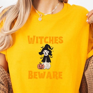 May include: A yellow t-shirt with a graphic of a dog wearing a witch's hat and holding a pumpkin. The text "Witches Beware" is printed on the shirt.